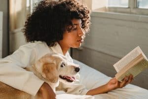 woman reading with her dog/why won't my dog leave me alone?